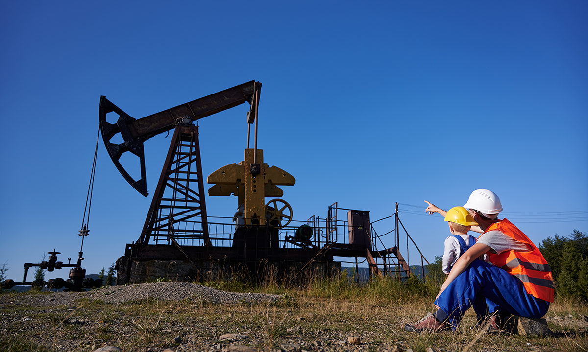 An oil worker points out a pumpjack for a young boy